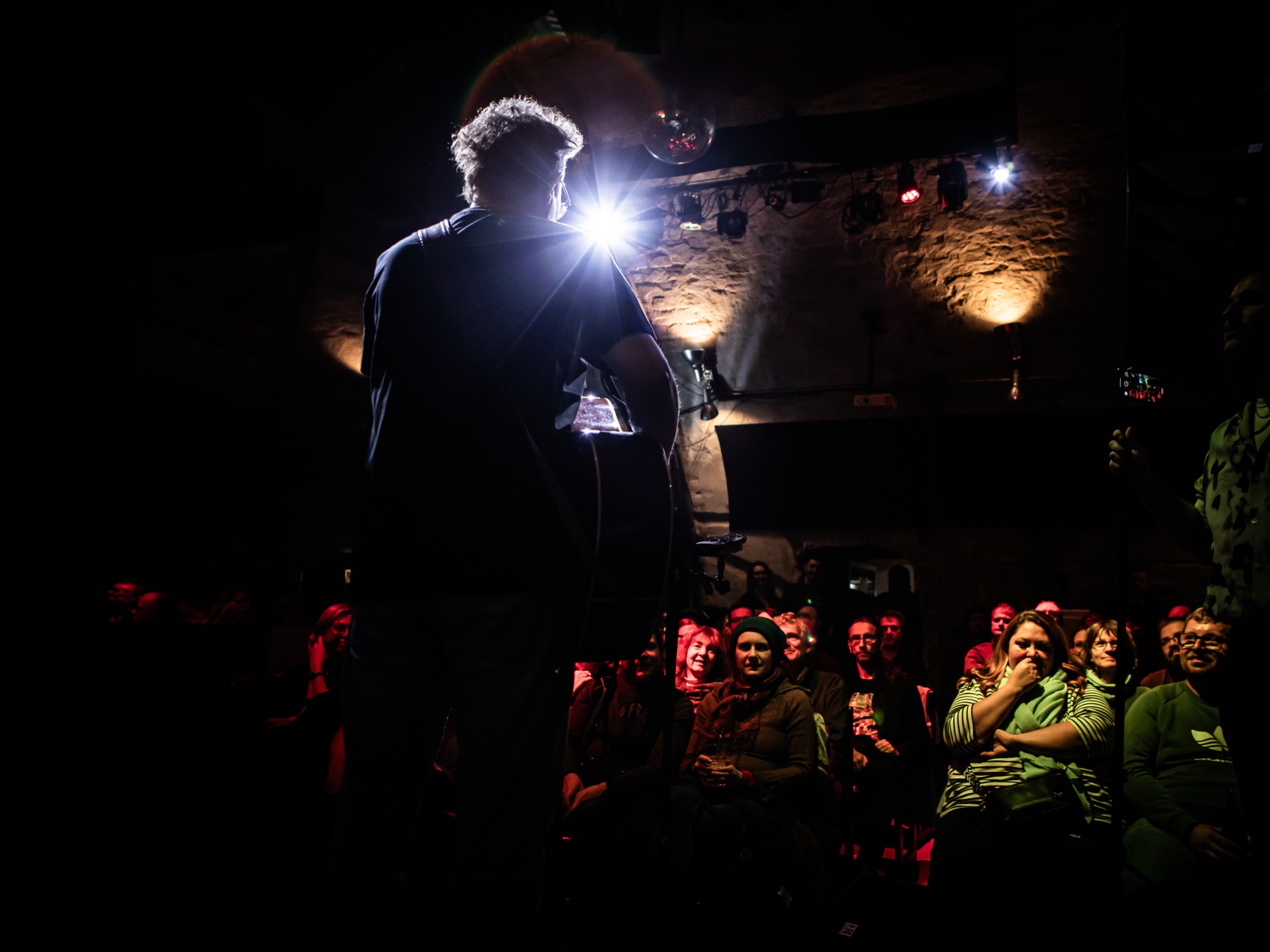 Melvin von hinten im Spotlight, vor einem lachenden Publikum