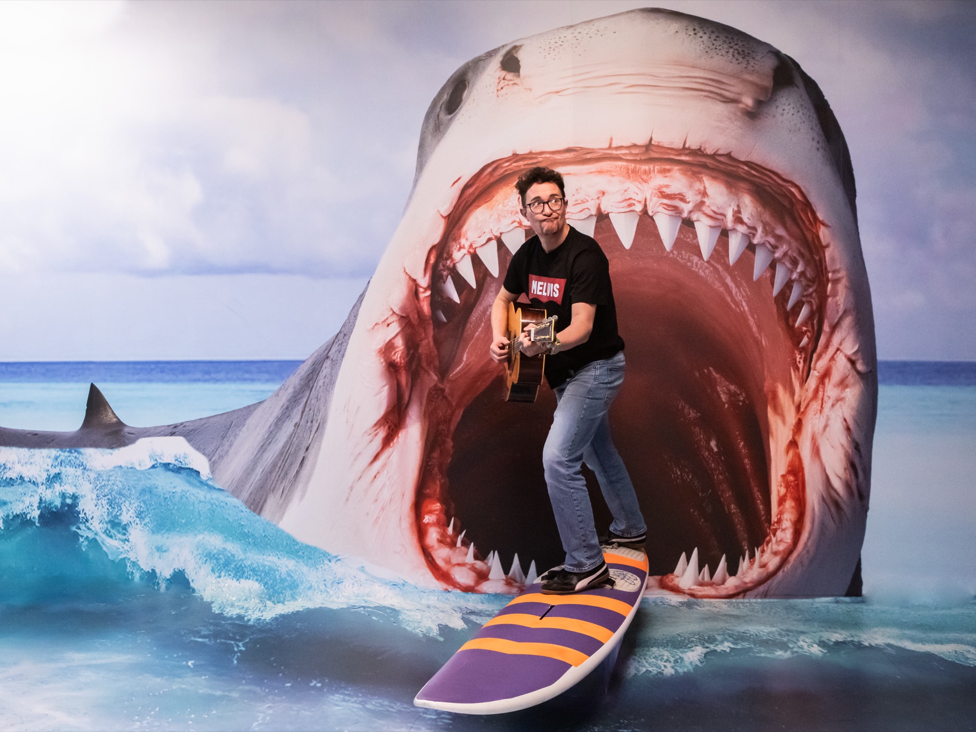 Melvin auf einem Surfbrett vor einem riesigen Hai